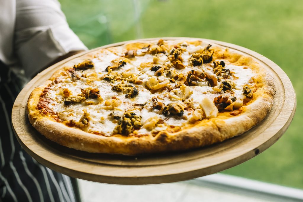 chef holding seafood pizza with shrimp mussels calamari squid and cheese